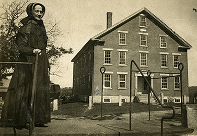 Shaker woman in front of North Family Trustees Office, Enfield, NH