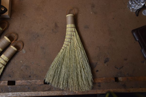 A small hand sized broom with brown cording